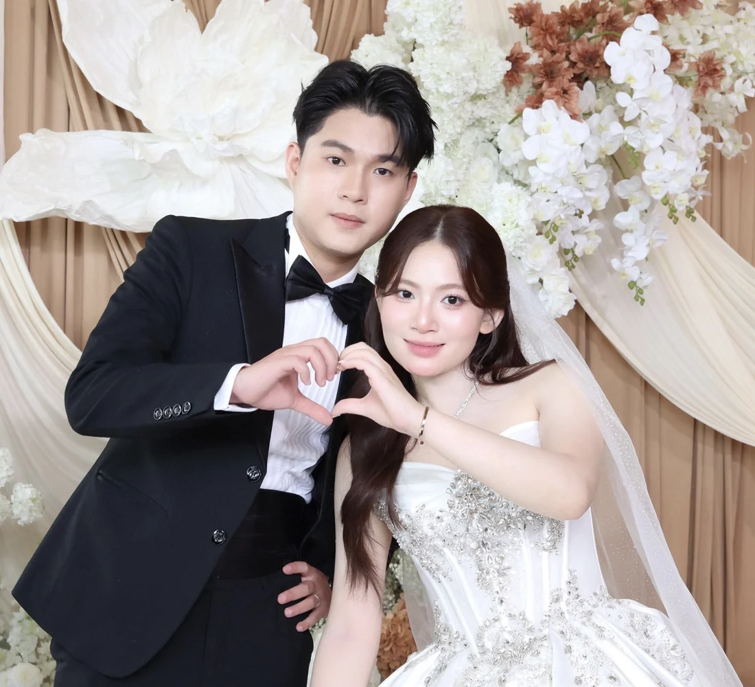 Cô dâu chú rể tạo hình trái tim trước backdrop hoa, ảnh chụp tại booth MOMENT26
