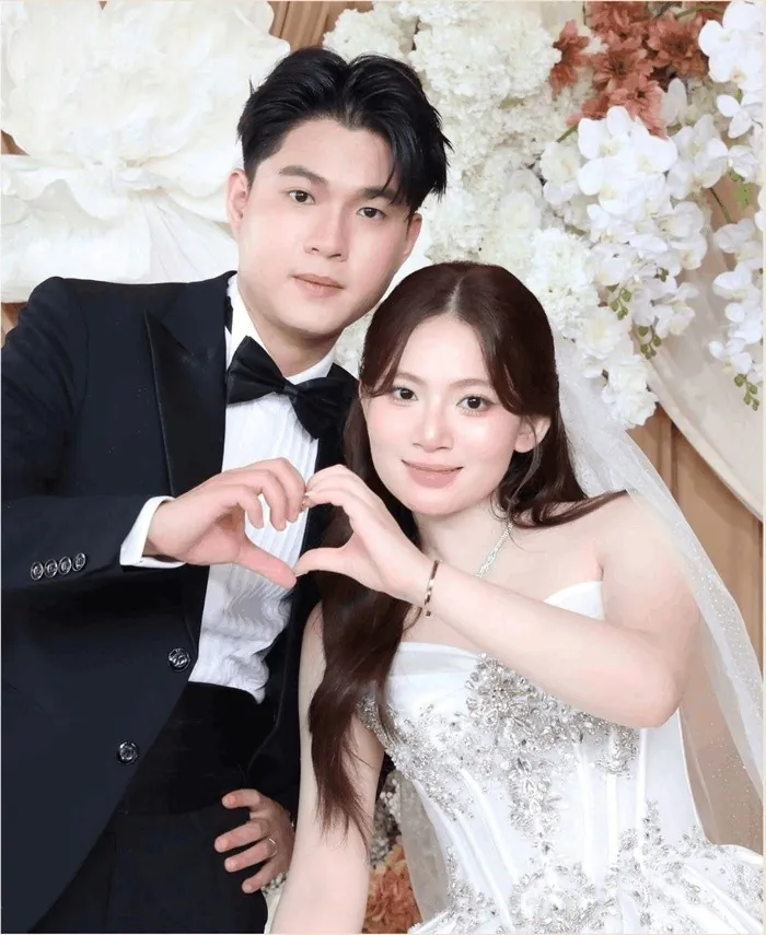 Cô dâu chú rể tạo hình trái tim trước backdrop hoa, ảnh chụp tại booth MOMENT26