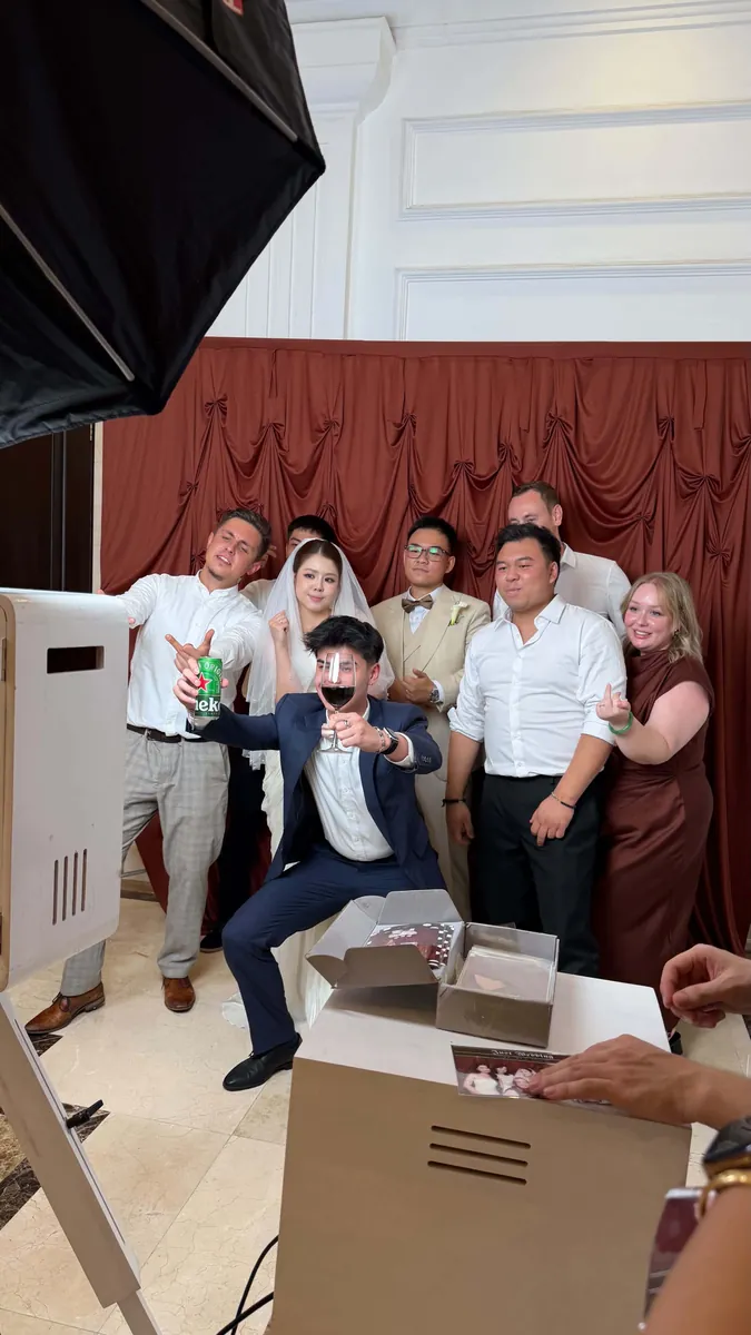 Khách mời cùng tạo dáng trước booth, nhân viên MOMENT26 lấy ảnh vừa in