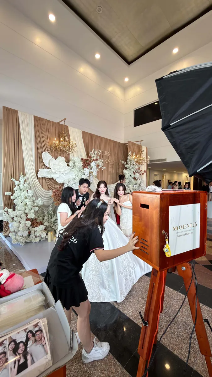Cô dâu chú rể và khách chụp ảnh trước booth gỗ trong sảnh tiệc