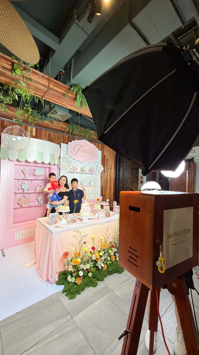 Booth gỗ cạnh bàn gallery hồng, các bé chụp ảnh phía sau