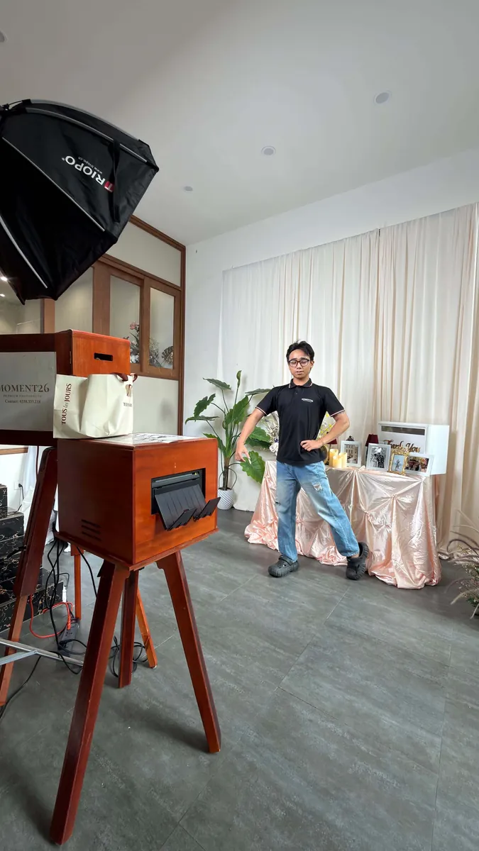 Nhân sự MOMENT26 tạo dáng thử ảnh bên booth gỗ và máy in