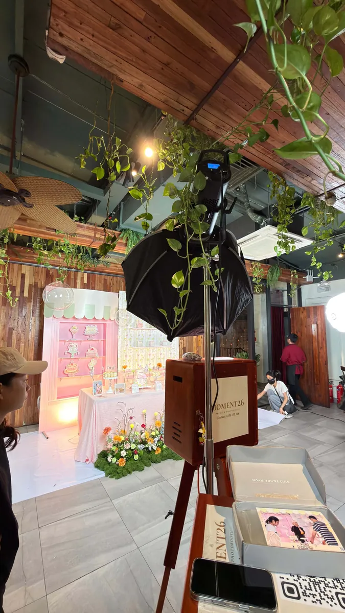 Booth gỗ, đèn và máy in đặt cạnh lối vào trang trí cây xanh