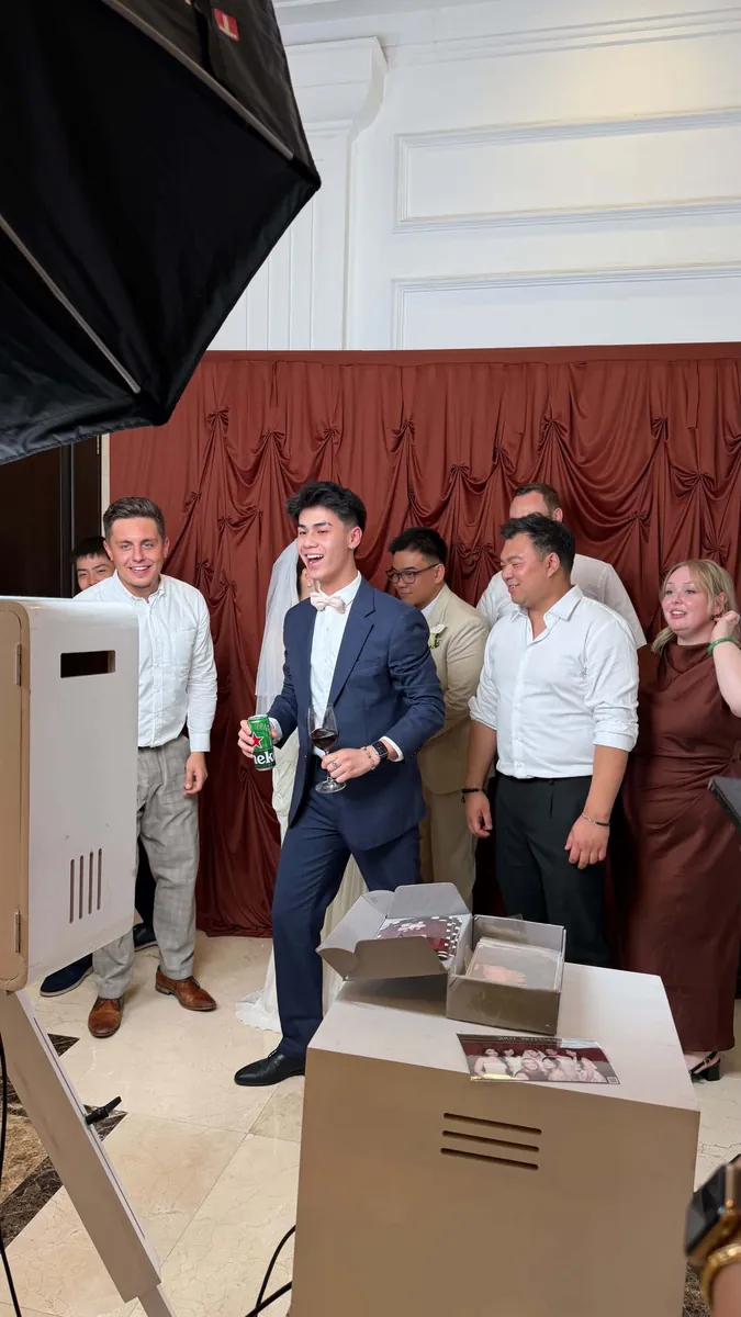 Chú rể và khách mời cười đùa trước backdrop đỏ