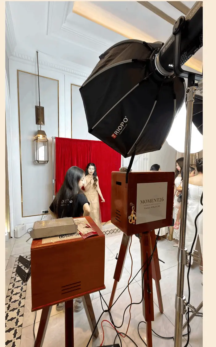 Khách chụp ảnh với backdrop đỏ, booth và đèn studio